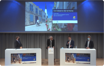 Participants à une conférence discutant sur scène avec un écran de présentation en arrière-plan, illustrant l'importance de la donnée pour le pilotage de l'action dans les territoires.